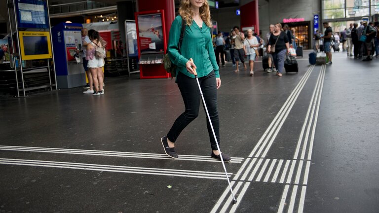 Une femme avec une canne d'aveugle à la gare. | © SBB CFF FFS/Flavia Trachsel